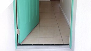 Un passadís amb una porta verda que condueix a una habitació amb sostre blanc i un llum.