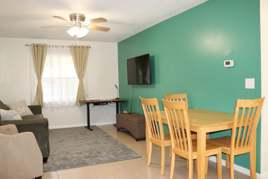 A living room with a green wall, a ceiling fan, a TV, a dining table with chairs, and a sofa.