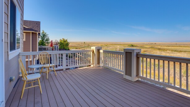 Una terraza de madera con dos sillas y una mesa pequeña, con vista a un paisaje llano.