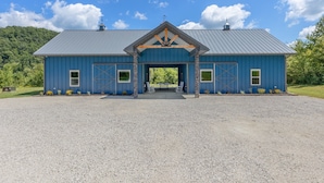 A blue barn with a metal roof, a central entrance, and a gravel driveway. - New Barndo/ATV Trailer Park/Outdoor Shower/HotTub (Stanton)