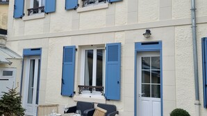A two-story building with blue shutters, a dining area with wooden furniture, and a potted plant. - Jolie Maison à 3 min de la Plage et au Pied des Commerces (Blonville-sur-Mer)