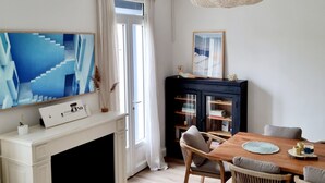 A modern living room with a fireplace, dining table, and chairs. There is a large TV mounted on the wall, a bookshelf, and a hanging light fixture. - Jolie Maison à 3 min de la Plage et au Pied des Commerces (Blonville-sur-Mer)