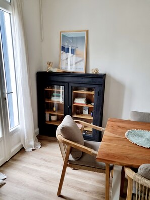 Une pièce comprenant une table à manger en bois, une chaise rembourrée, un buffet noir aux portes vitrées et un tableau encadré placé au-dessus du buffet.