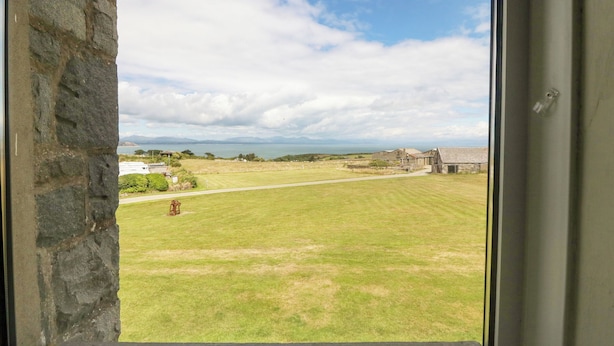 A view from a window overlooking a grassy field with a stone wall on one side and a building in the distance. - Cim Canol (Pwllheli)