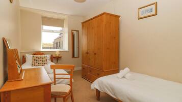 Un dormitorio con un escritorio de madera, una silla, una cama, un armario, una ventana y un espejo.