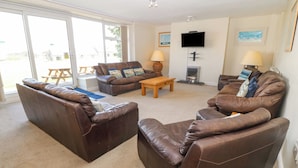 A living room with leather sofas, a wooden coffee table, a flat-screen TV mounted on the wall, and a fireplace. - Cim Canol (Pwllheli)