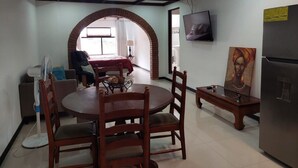 A dining area with a round table and chairs, a TV mounted on the wall, and a refrigerator.