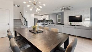 Moderni olohuone, jossa on puinen ruokapöytä, harmaat sohvat, televisio ja kattotuuletin.