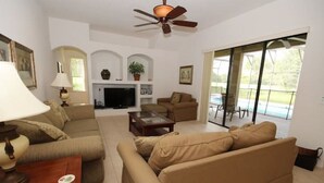 A living room with a sofa, coffee table, TV, and a ceiling fan. There is a sliding glass door leading to a patio. - Mushu's Temple 122LP (Davenport)