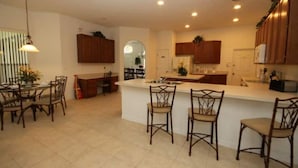 A modern kitchen with a central island, wooden cabinets, and a dining area with chairs. - Mushu's Temple 122LP (Davenport)