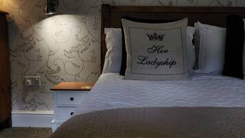 A bedroom with a patterned wallpaper, a decorative wall piece, a bedside lamp, a nightstand, and a bed with a pillow featuring the text "Her Ladyship".