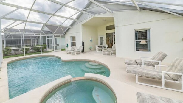 A pool area with a glass ceiling, lounge chairs, and a small table.