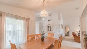 A spacious dining area with a wooden table and chairs, a chandelier, and a view of a living room in the background.