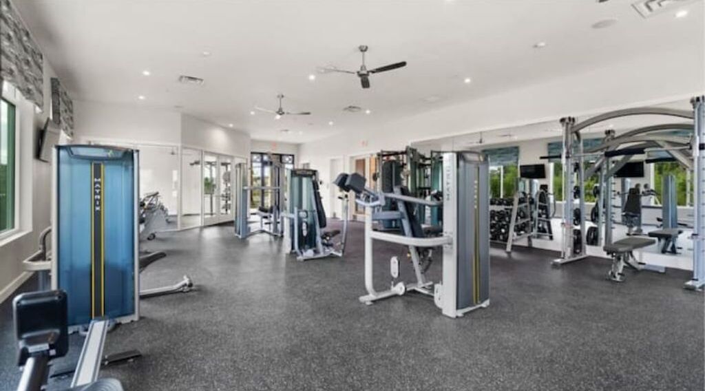 A modern gym with various exercise machines, a blue weightlifting station, and a ceiling fan.