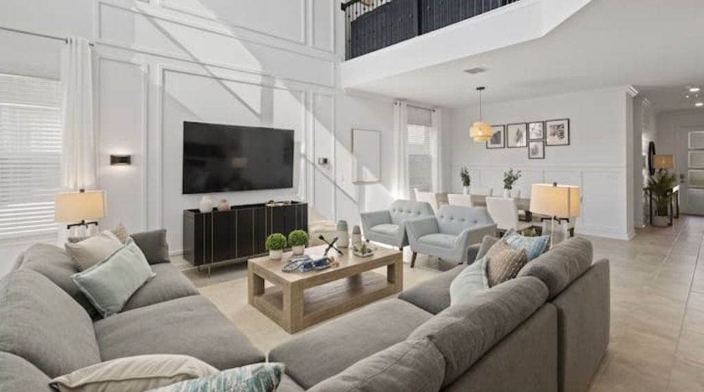 A spacious living room with a large TV, grey sofas, a wooden coffee table, and a staircase leading to an upper level.