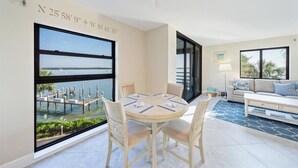 A room with a dining table and chairs, a sofa, and large windows offering a view of a dock and water. - COMPLETELY REMODELED Luxury Riverside 1BR Condo: Panoramic River Views (Marco Island)