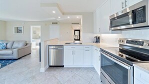 A modern kitchen with stainless steel appliances, white cabinetry, and a central island. - COMPLETELY REMODELED Luxury Riverside 1BR Condo: Panoramic River Views (Marco Island)