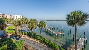 A marina with docks, palm trees, and a building in the background. - COMPLETELY REMODELED Luxury Riverside 1BR Condo: Panoramic River Views (Marco Island)