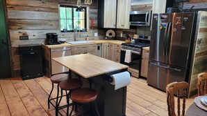 Una cocina moderna con detalles de madera, una isla central con taburetes, electrodomésticos de acero inoxidable y un ventanal que proporciona luz natural.