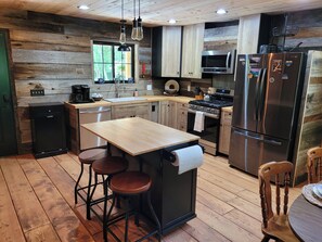 A modern kitchen with wooden accents, a central island with stools, stainless steel appliances, and a window providing natural light. - New River Gorge National Park,1 mile to AOTG (Victor)