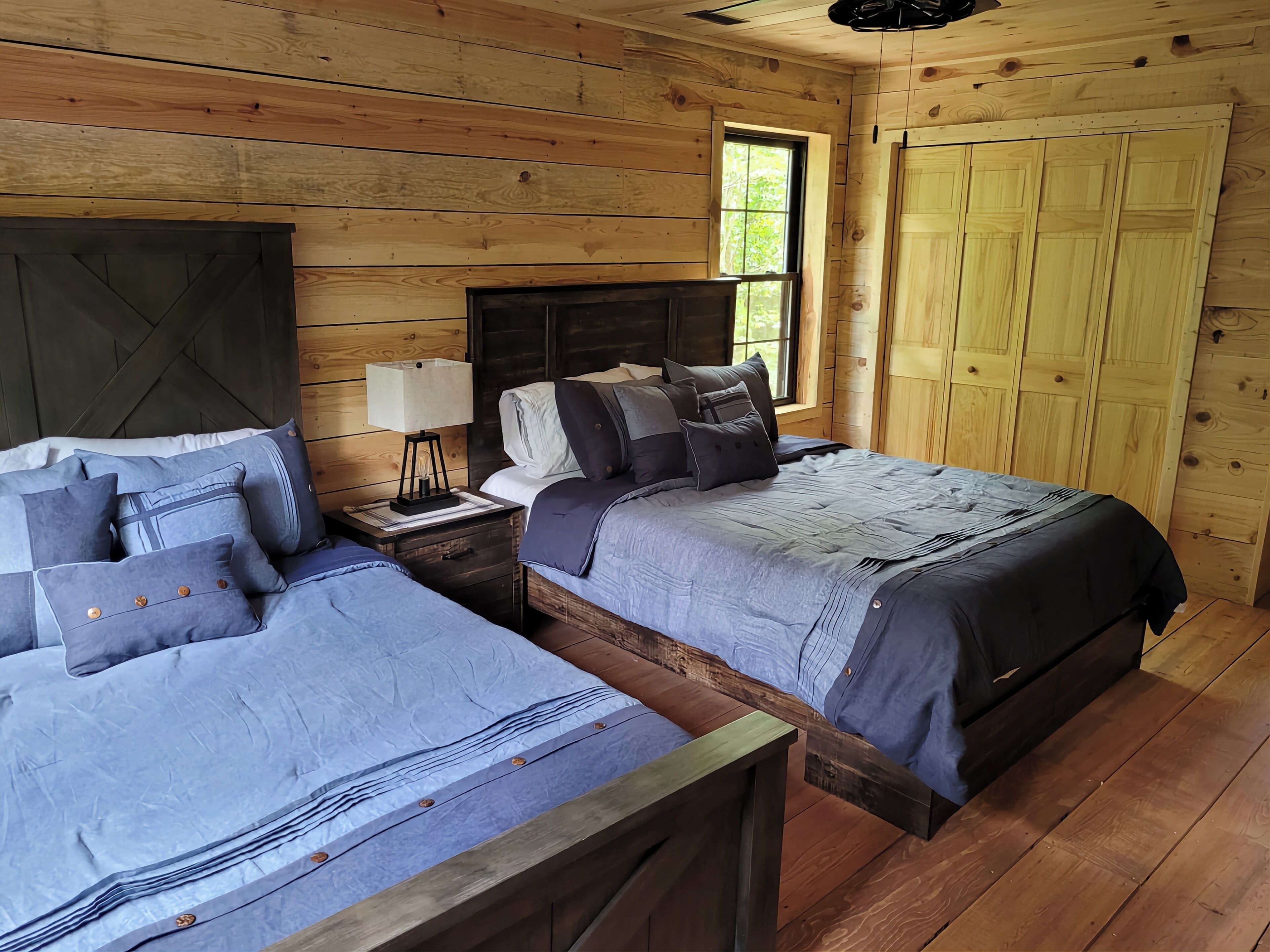 Ein Schlafzimmer einer Holzhütte mit zwei Betten, einem Nachttisch, einem Fenster und einem Kleiderschrank.