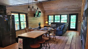 Una cocina acogedora de estilo cabaña con interior de madera, un comedor con taburetes y un ventanal con vistas al exterior.
