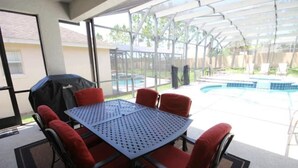 Un patio techado con piscina, sillas rojas y una mesa.