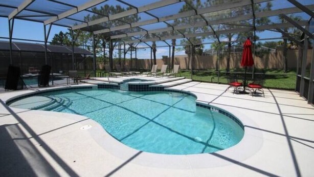 Una piscina exterior techada con una estructura de sombrilla, sillas de descanso y una sombrilla roja.