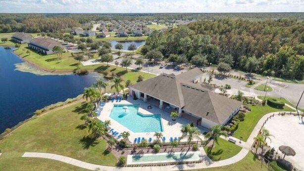 A large house with a swimming pool, surrounded by a well-maintained lawn and palm trees. - Pool Home in Resort Community (Kissimmee)