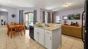 A modern kitchen with a dining area, a built-in island, and a living area with a sofa and TV. - Pool Home in Resort Community (Kissimmee)