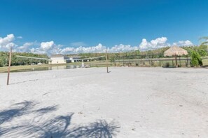 Una cancha de voleibol de playa con una red, una estructura de techo de paja y un edificio al fondo.