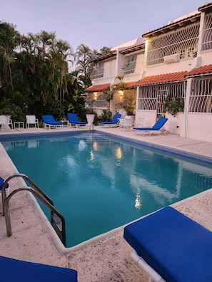 A swimming pool with blue lounge chairs and a white building with red-tiled roofs. - Fabulous, spacious condo with pool, 5 mins from Mullins Beach. (Mullins)