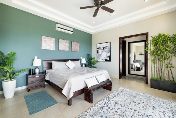 Une chambre à coucher avec un lit, des tables de chevet, un ventilateur de plafond et une grande fenêtre.