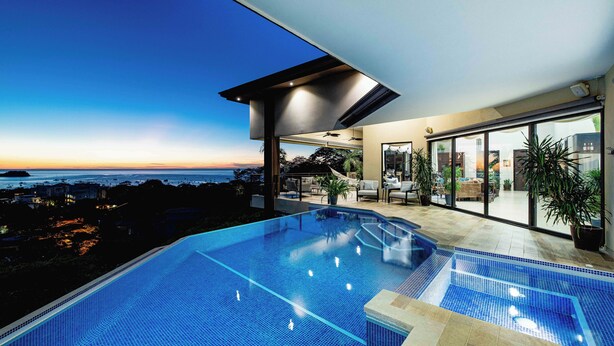 Una piscina infinita moderna con vista al océano al atardecer.