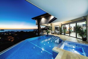 Une piscine à débordement moderne offrant une vue sur l’océan au crépuscule.