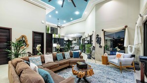 A spacious living area with a sectional sofa, a round coffee table, and a large window. - Luxury Ocean View Above Coco Beach - Concierge + Hot Tub + Daily Housekeeping (Playas del Coco)