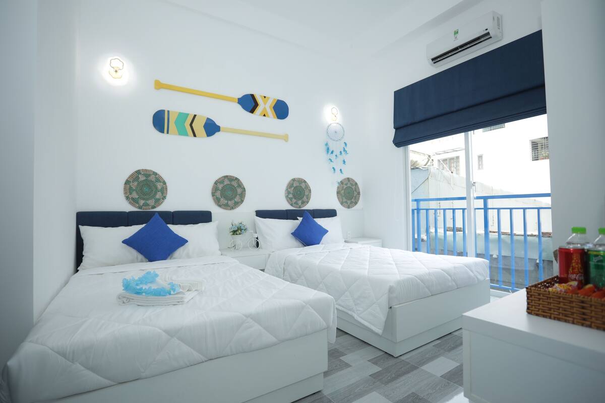 A hotel room with two beds, a small table, and a balcony.