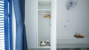 A white closet with a hanging rack, a basket, and a fan on the wall. - TNJ TASMANIA HOTEL (Da Nang)