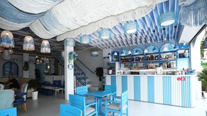 A bar area with blue chairs and tables, a staircase, and a counter with various bottles. - TNJ TASMANIA HOTEL (Da Nang)