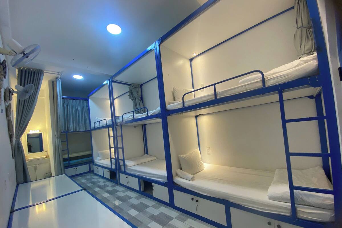 A dormitory room with bunk beds, a small table, and a mirror.