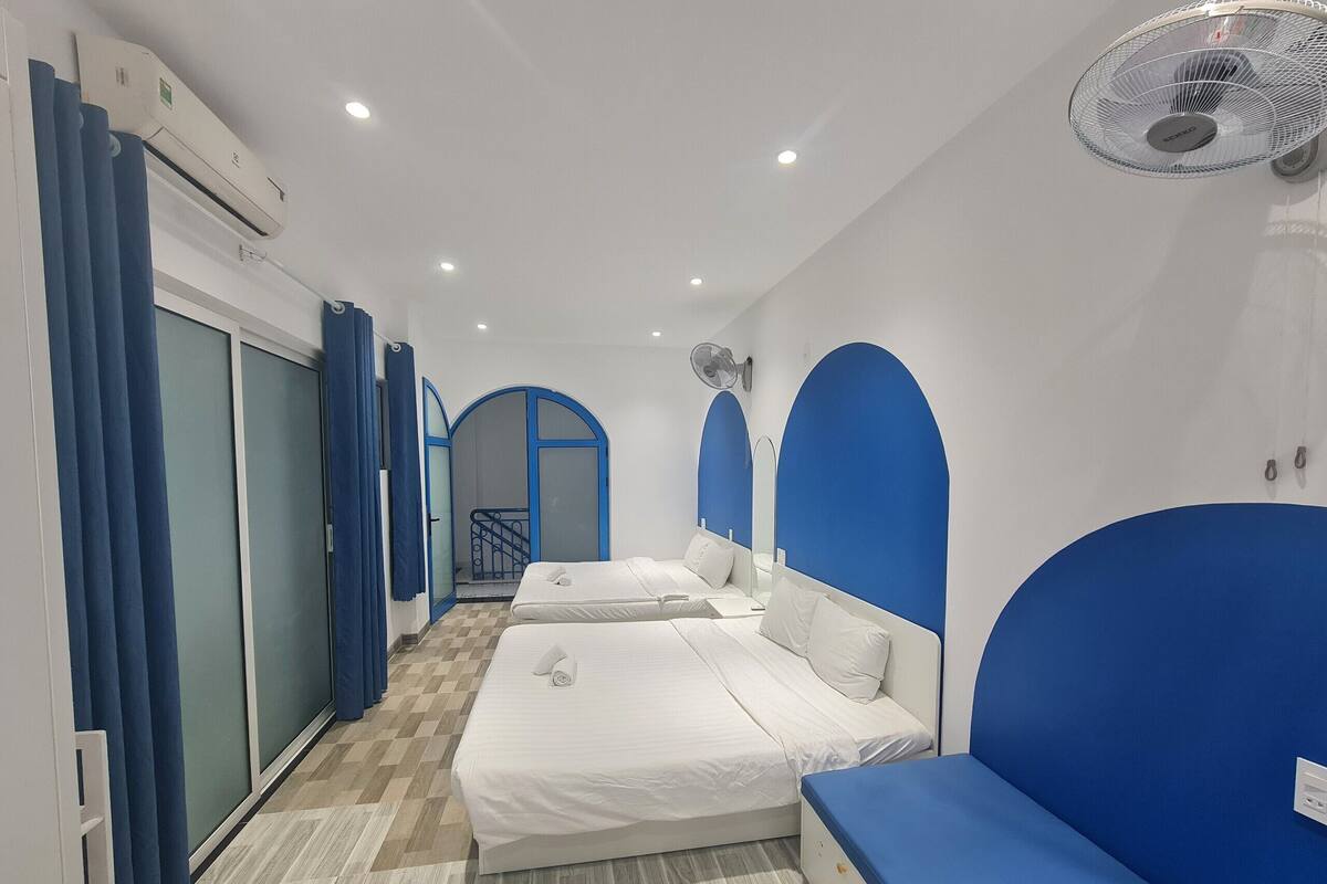 A hotel room with two beds, a blue accent wall, a ceiling fan, and a staircase leading to another room.