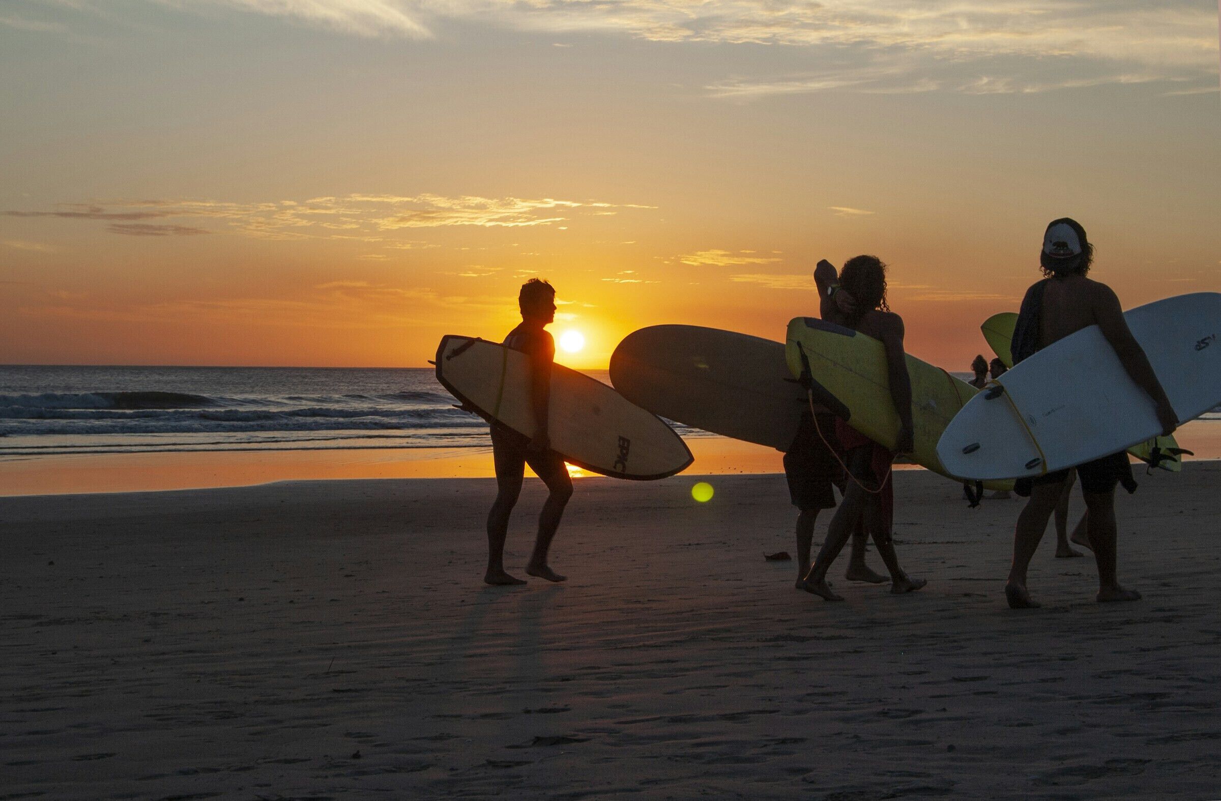 En strandscene med mennesker, der bærer surfboards i solnedgangen.