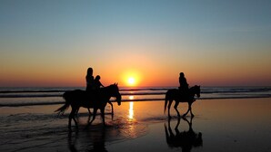 Silhouetten zweier Reiter auf Pferden am Strand bei Sonnenuntergang.