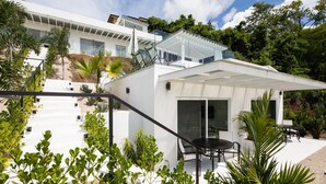Ein modernes Haus mit weißer Fassade, einer überdachten Sitzgruppe im Freien und einer Treppe zu einer zweiten Ebene.