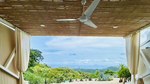 Eine Terrasse im Freien mit Deckenventilator, Blick auf einen Strand und einer Holzterrasse.
