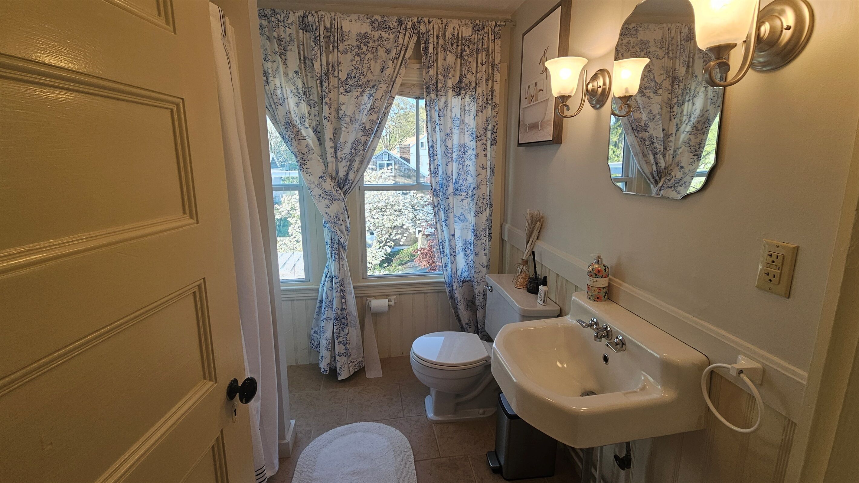 Un bagno con il water, lavandino e finestra con tende a fiori.