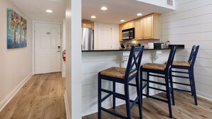Una cocina con gabinetes de madera, un refrigerador de acero inoxidable, un microondas y dos taburetes de bar.