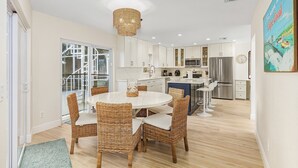 Una cocina moderna con armarios blancos, electrodomésticos de acero inoxidable y un comedor con sillas de mimbre y una mesa blanca.