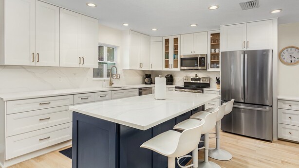 Una cocina moderna con armarios blancos, electrodomésticos de acero inoxidable y una isla central con taburetes de bar.