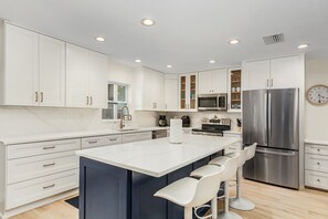 A modern kitchen with white cabinets, stainless steel appliances, and a central island with bar stools.
